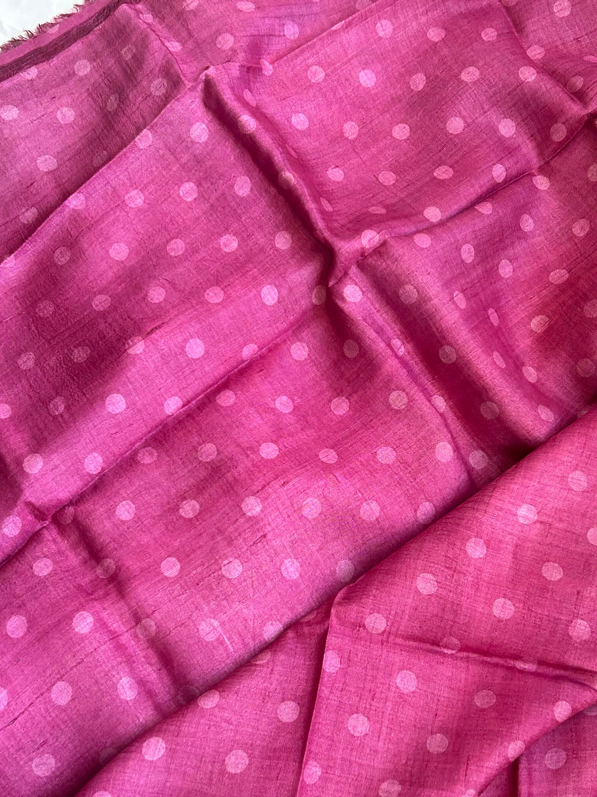A close-up of a pink fabric blouse matching to pallu, with a repeating light pink polka dot pattern, shown in soft folds.