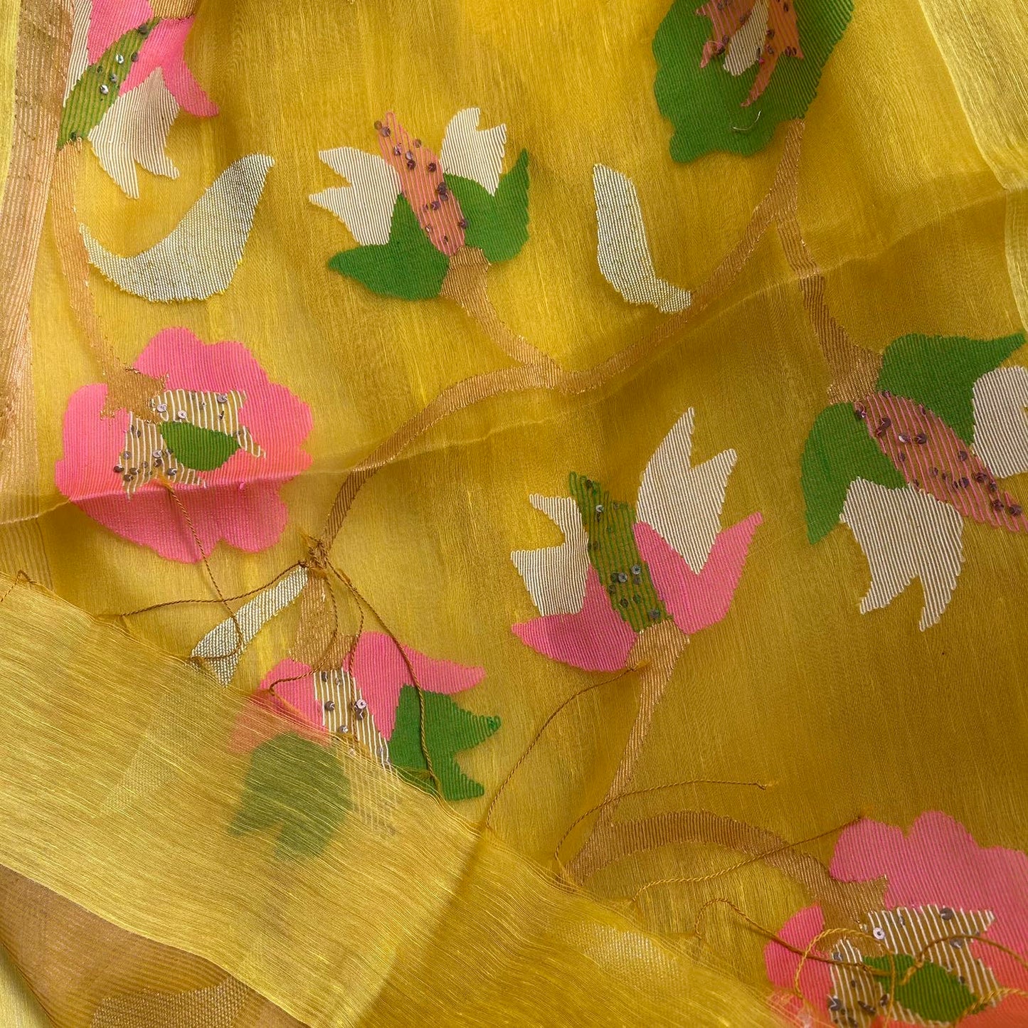 A close-up of a yellow sheer fabric, likely organza or silk, decorated with embroidered floral motifs in pink, white, and green.